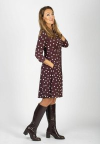 Brązowa sukienka w białe groszki z rękawami do połowy łokcia, z dopasowanym górnym krojem, rozkloszowanym dołem i bocznymi kieszeniami. Do tego brązowe kozaki za kolano.