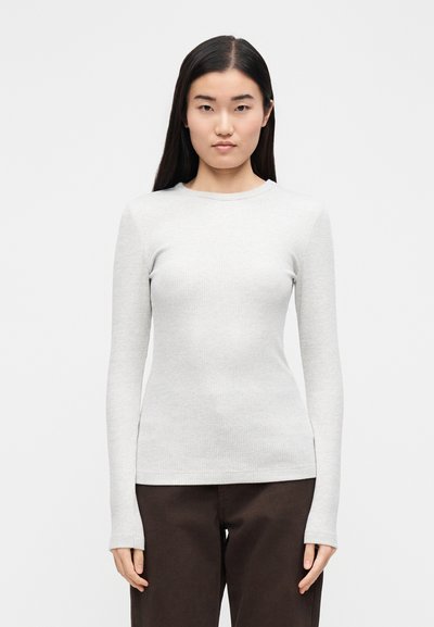 Helehall pika varrukaga soonikkoes särk ümarliku kaelusega ja keha järgiva lõikega, kantud tumepruunide pükstega. Pehme tekstuur ja sile välimus.