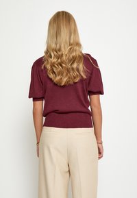 Bordeaux brei-top met korte, geplooide mouwen en geribde tailleband, gecombineerd met beige wijde broek met pocketdetails.