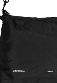 Czarna torba z nylonu z teksturowaną powierzchnią, regulowanym paskiem, wytłoczonym napisem "10" oraz słowami "NIESPODZIEWANIE" i "PROSTE" w białym kolorze.