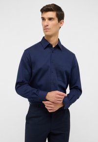 Donkerblauw overhemd met lange mouwen, knoopsluiting aan de voorkant, kraag en borstzak. Glad textuur en slim fit ontwerp. Zwarte knopen.