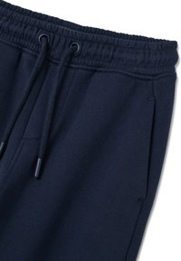 Marineblauwe sweatpants met een tailleband van elastiek en een trekkoord, tonen de bovenkant met de zijzaknaad en metalen uiteinden van het trekkoord.