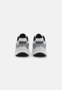 Skechers tenisky s bílým síťovaným svrškem, šedými detaily, černou patou a strukturovanou podrážkou. Obsahují logo na patě a polstrovaný límec.