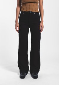 Jeans acampanados de talle alto en negro con una textura suave y bolsillos frontales, que cuentan con un botón de metal y detalles de costura en contraste.