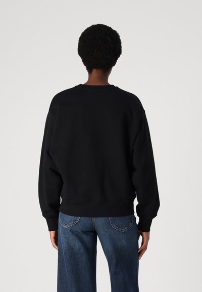 Felpa nera con scollo rotondo, spalle cadenti e polsini a costine. Abbinata a jeans in denim chiaro a vita alta.