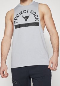 Camiseta sin mangas de color gris claro con escote redondo, que presenta un gráfico negro de "PROJECT ROCK" y un logo de toro en el pecho. Textura suave.