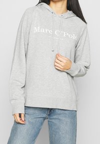 Sudadera gris hecha de una suave mezcla de algodón, con capucha ajustable y texto de logo en blanco, puños y dobladillo acanalados, corte relajado.