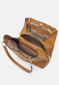 Kabelka z hladké tan kůže s texturovaným povrchem, zlatými detaily a prostorným, podšívkovým interiérem, který obsahuje jednu kapsu na zip a magnetické zapínání.