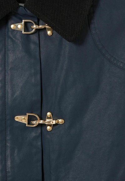 Veste imperméable bleu marine avec un col en velours côtelé noir, des fermetures métalliques dorées et une texture de tissu lisse et brillante.
