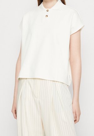 Witte polo met korte mouwen en twee gouden knopen bij de kraag, met een losse pasvorm en een gladde textuur. Gecombineerd met licht gestreepte broek.