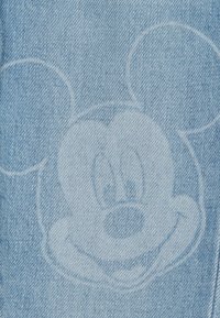Verblasster Mickey-Maus-Gesichtsprint auf hellblauem Denim-Stoff, der die Ohren und den lächelnden Ausdruck des Charakters zeigt.