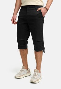 Svarte cargo shorts med sidelommer, rullede cuffs og rette ben. Brukt sammen med lyse sporty joggesko.