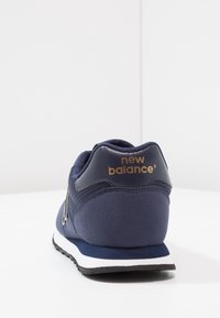 Mörkblå sneakers med mesh och mocka, vit mellansula, vadderad krage och guldlogotyp på hälen. Klassisk atletisk design.