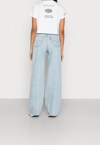 Jeans de tiro medio de denim en un tono azul claro y de pierna ancha, con bolsillos traseros cosidos, combinados con una camiseta recortada blanca.