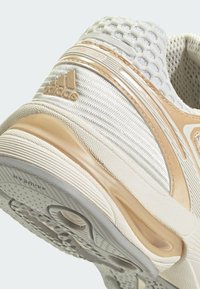 Gaišbeige sporta apavi ar acs audumu, teksturētām akcentiem un gumijas zoli. Iekļauj Adidas logo un mīkstinošu papēdi atbalstam.