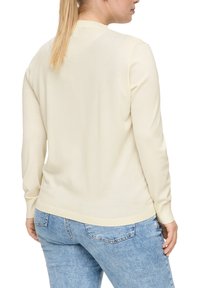 Hellbeiges Sweatshirt aus weichem Strickmaterial, mit rundem Halsausschnitt und gerippten Bündchen. Kombiniert mit hellblauen Jeans.