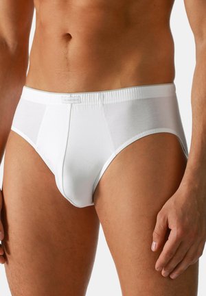 Uomo che indossa slip di cotone bianchi semplici, in piedi con le braccia rilassate lungo i fianchi su sfondo bianco.