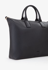 Borsa tote in pelle nera con una finitura texturizzata, dotata di due manici robusti e un design minimalista. Accessori in metallo dorato valorizzano la cerniera.