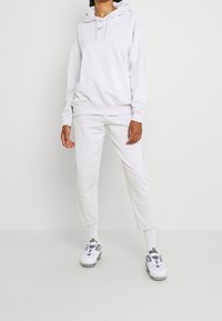 Ljusgrå hoodie med dragsko och logotyp, matchad med tapered sweatpants och vita sneakers. Mjuk och slät textur genom hela plagget.