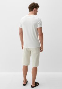 Weißes kurzärmliges T-Shirt, lässiger Schnitt, kombiniert mit hellen Shorts und schwarzen Flip-Flops. Glatte Stofftextur, minimalistisches Design.