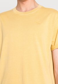 Yellow cotton t-shirt with a crew neck, short sleeves, and a subtle tonal logo on the chest. Soft texture with a relaxed fit.