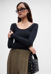 Musthave musta pikasleeveline topp, millel on ümar kaelus; kõrge vöökoht, tekstuursed pruunid püksid; must kott hõbedasten nukkudega, mida hoitakse ühes käes.