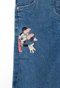 Jeans de mezclilla en azul con una textura desgastada. Presentan un diseño impreso de un personaje de dibujos animados con un lazo rosa, con los brazos extendidos, en el muslo.