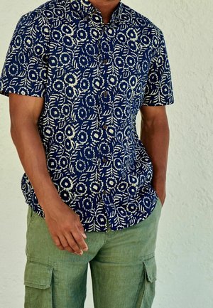 Korte mouwen overhemd in marineblauw met een wit bloemenpatroon, gecombineerd met lichtgroene cargo pants met zijzakken en een ontspannen pasvorm.