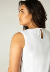 Witte mouwloze top met een ronde halslijn, voorzien van een sleutelgatdetail aan de achterkant en een gladde stofstructuur.