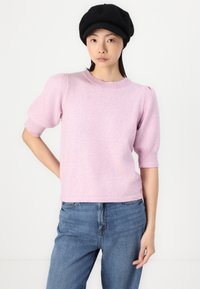 Light pink knit sweater with short, ribbed sleeves and a crew neckline. Worn with blue denim jeans. Accented with a black beret.