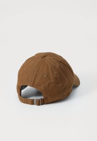 Boné de basebol de algodão marrom com aba curva, tira ajustável na parte de trás e design de seis painéis com ilhós de ventilação.