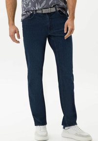 Mörkblå denimjeans med rak skärning, femficksdesign och subtila stygn, som bärs med ett ljusgrått bälte och vita sneakers.