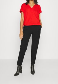 Czerony top z dekoltem w kształcie litery V i krótkimi rękawami, zestawiony z czarnymi zwężającymi się spodniami i czarnymi botkami w szpic. Gładka tekstura i dopasowany fason.