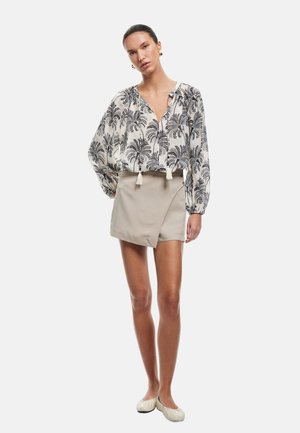 Blouse légère à motifs avec un design de palmiers noirs sur fond blanc, associée à une jupe portefeuille beige, complétant une tenue décontractée.