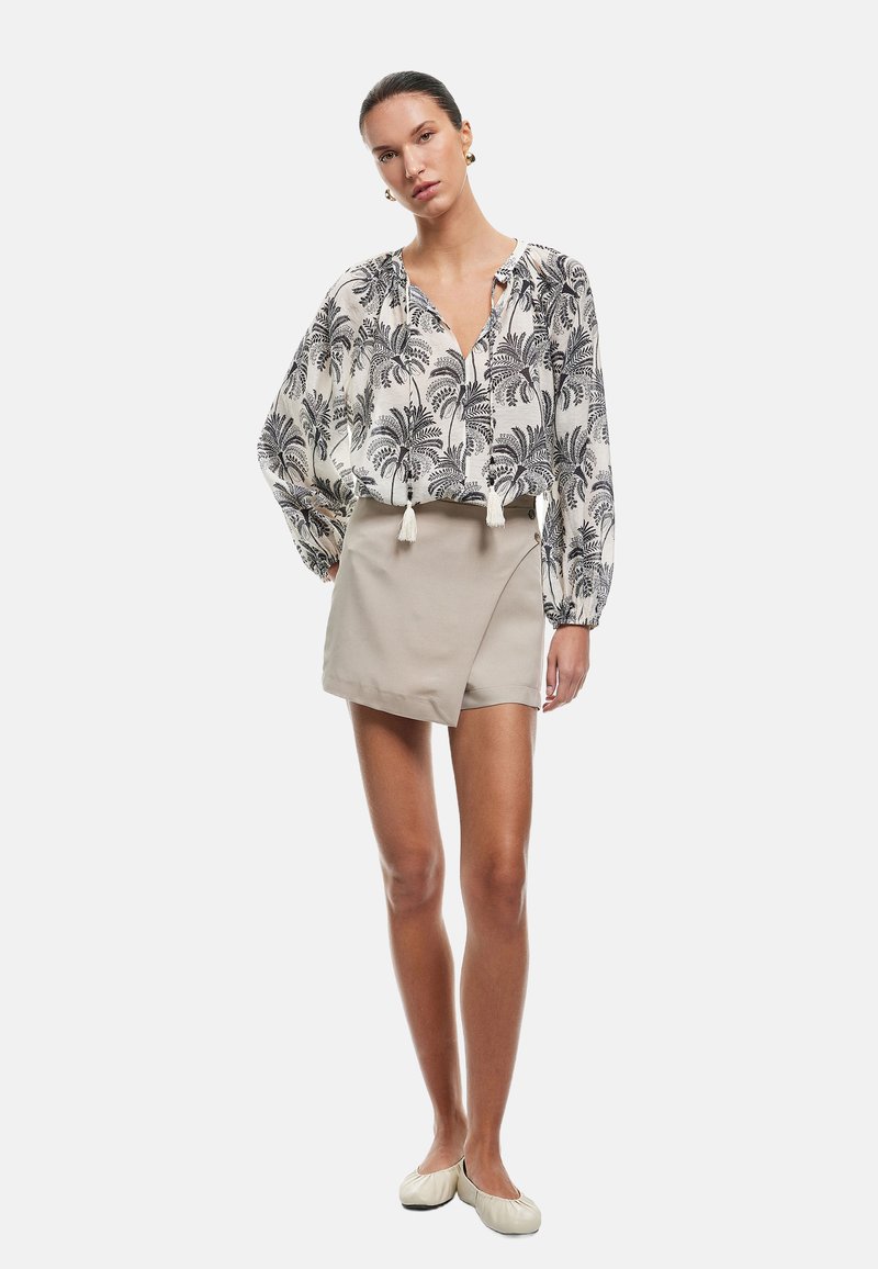 Blusa ligera y estampada con diseño de palmeras en negro sobre fondo blanco, combinada con una falda envolvente beige, que completa un atuendo casual.