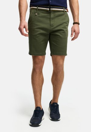 Olive green shorts made from cotton, featuring a classic cut, belt loops, and a striped belt. Worn with navy sneakers.