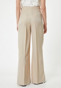 Beige wijde broek met een getailleerde pasvorm, met plooien, een soepele textuur en een hoge taille. De achterkant benadrukt strakke lijnen.