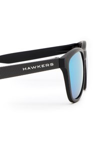 Ochelari negri de soare cu un model texturat pe brațe, lentile reflective albastre și marca "HAWKERS" pe lateral.