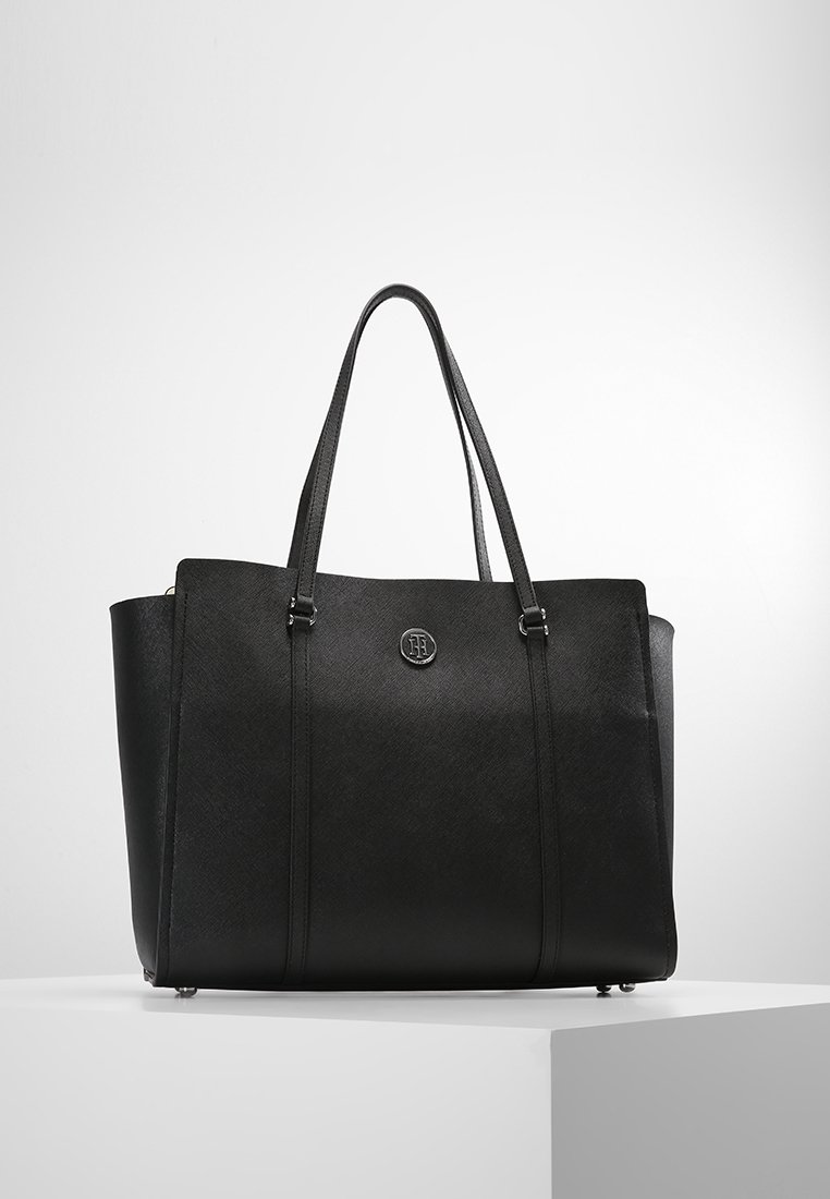 Sac cabas en cuir noir avec finition texturée, doubles poignées supérieures, coutures verticales et emblème de marque sur le devant. Conception spacieuse.