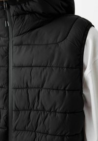 Czarna pikowana kamizelka z wysokim kołnierzem, z przeszywanymi sekcjami i przednim zamkiem błyskawicznym, wykonana z gładkiego, lekkiego materiału.