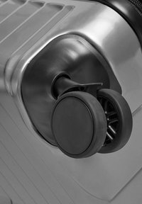 Schwarzes Rad eines Hartschalenkoffers mit rundem Design und strukturierter Oberfläche, befestigt an einem metallischen Fuß mit glatter Oberfläche.