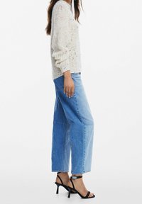 Pull en maille beige clair avec des éclats multicolores, associé à un jean large bleu clair et des sandales à talons noires à lanières.