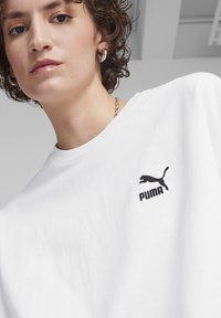 Hvid bomulds t-shirt med et sort broderet Puma-logo på venstre bryst. Rund halsudskæring, blød tekstur, afslappet pasform.