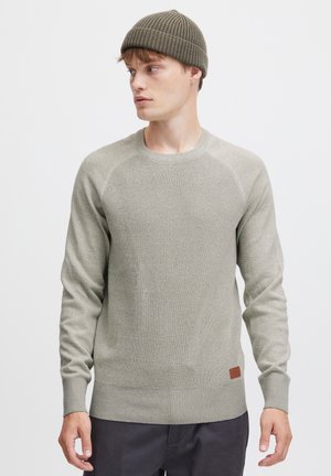 Suéter de punto gris claro con detalles acanalados, cuello redondo y puños acanalados. Llevado con un gorro acanalado a juego. Acento de etiqueta marrón cerca del dobladillo.