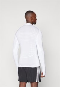 Langärmliges Sportshirt in Weiß mit strukturiertem Rautenmuster, elastischem Stoff und ergonomischem Design für verbesserten Sitz und Beweglichkeit.