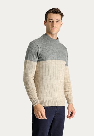 Suéter de punto con un cuello alto, textura acanalada y diseño en bloques de color en gris claro, gris oscuro y crema. Corte clásico con mangas largas.