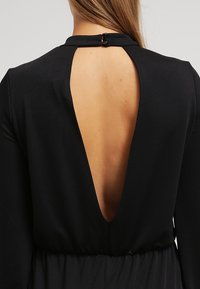 Vestido negro con escote en forma de V profundo en la espalda, mangas largas y cintura ceñida. Fabricado en tejido texturizado con un acabado suave.