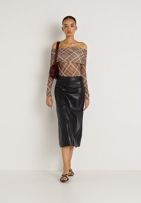 Plecu rajonā atklāta apdrukāta topiņa bēšā un brūnā krāsā, kombinēta ar piegulošu melnu ādas midi svārku un melnām plakanām sandālēm. Izcelts ar nelielu tumši sarkanu somiņu.