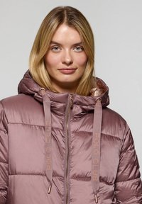 Giacca imbottita con cappuccio in morbido tessuto malva con finitura lucida. Presenta una chiusura frontale con zip, cordini con marchio e texture trapuntata.