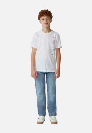 Witte katoenen t-shirt met grafische print aan de linkerkant, gecombineerd met lichtblauwe spijkerbroek en witte sneakers met tan kleurige zolen.